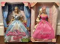 Front view of the two Barbie dolls in original unopened packaging showing Sleeping Beauty in blue gown and Rapunzel in pink dress with crown.