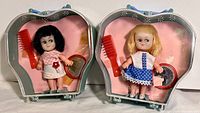 Two Cutie Pie dolls in their original apple-shaped plastic packaging with hair comb and mirror accessories visible.