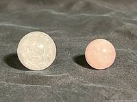 Two polished quartz spheres on a dark surface, showing the white quartz sphere on left and smaller pink quartz sphere on right.