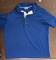 Blue BMW golf shirt laid flat on wood surface showing front side with zippered collar and white inner collar trim