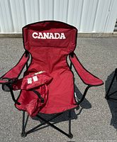 Front view of red folding camping chair with 'CANADA' printed on backrest alongside the carrying case placed on seat.