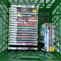 Top-view photo of a green basket filled with empty Xbox 360 and Xbox original video game cases arranged standing upright.