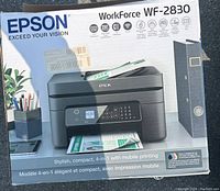 Photo of the Epson Workforce WF-2830 printer in original box showing front of the box with printer image and key features.
