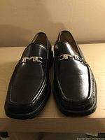 Front view of pair of black leather Bruno Magli men's dress shoes with metal M logo on top.
