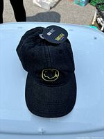 Photo of a black Nirvana baseball hat with the iconic yellow smiley face logo embroidered on the front. The hat appears new with tag attached.