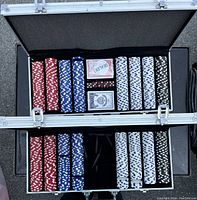 Open poker chip case showing four columns of poker chips in red, blue, white, and black. Two decks of playing cards and two sets of dice are placed in compartments within the case, on a foam interior lining.