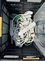 Photo of several white electronic power bars with cords tangled inside a container showing different sizes and some with switches.