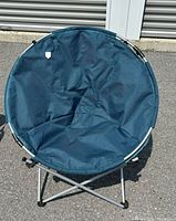 Blue round camping folding chair with a foldable metal frame sitting outdoors on pavement.
