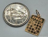 Photo showing the 10k gold bingo charm next to a quarter for scale. The charm spells out 'BINGO' on the top row and 'I LOVE U' in the card grid.