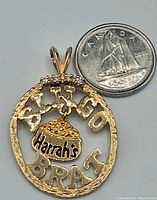 Front of circular gold pendant with “Bingo Brat” text, central Harrah’s bingo chip motif in gold, four diamonds set at top, shown next to Canadian dime for scale