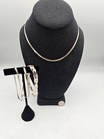 Photo of the sterling silver chain necklace displayed on a black bust and three silver bracelets on a black stand.