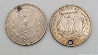 Reverse side of two 1921 American silver Morgan dollars, one with a hole near the rim, one intact