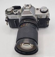 Front view of Canon AE-1 camera body with attached lens showing the model on the prism hump and lens barrel details.