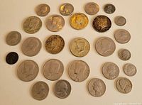 Top-down view of 26 American coins arranged in rows showing various denominations including half dollars, quarters, dimes, nickels, and pennies predominantly from the 1960s.