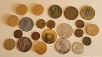 Top down photo of mixed coins, tokens, and wooden nickels arranged on a beige background, showing a variety of materials, sizes, and designs.