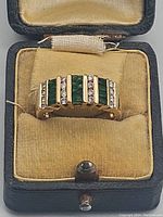Top-front view of ring in velvet-lined presentation box showing alternating emerald and diamond rows
