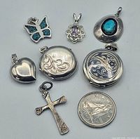 Photo showing all seven sterling silver pendants including lockets, butterfly, flower pendant with amethyst-colored stone, heart, cross, and turquoise set pendant along with a Canadian quarter for scale.