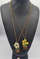 Front view of two gold-tone enamel flower pot pendants on chains displayed on necklace bust.