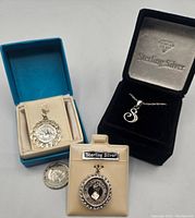 Lot includes two sterling silver charms and one pendant with an 18-inch chain, displayed in jewelry boxes with a quarter for scale.