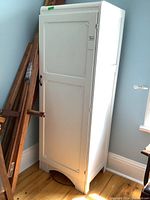 White painted antique armoire closed view showing front and side with carved trim details at top and on door panel.