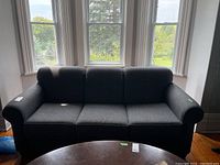 Full view of gray upholstered couch with wooden legs positioned in front of windows.