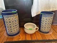 Three items: two decorative ceramic crocks and one white ceramic chamber pot. The crocks have a detailed blue and white floral geometric pattern; chamber pot is plain white with handle.