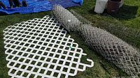 Two rolls of wire fencing lying on grass beside a white lattice panel and tomato cages.