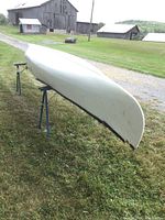 Side view of the underside of the white fiberglass canoe showing wood trim damage at hand and hull condition