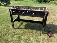 Full view of Barrington foosball table standing on grass. Features wooden handles on metal rods and black legs with branding.