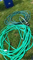 Two coiled green rubber garden hoses lying on grass, one lighter green and one darker with sprinkler attachment