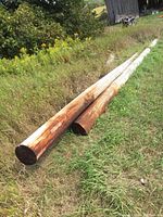 Five long wooden hydro poles on grass, showing length and natural wood finish with weathering.