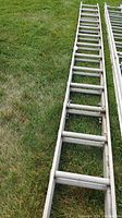 Full length side view of aluminum extension ladder laid flat on grass, shows overall length and condition.