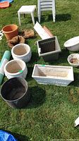 Sunlit view of all assorted planters and gardening accessories arranged on grass including cement, ceramic, plastic planters and liners with a roll of underlay