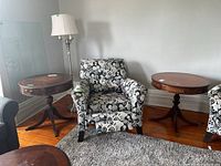 Two wood side tables with rounded tops flanking a patterned armchair, showing their general shape and size.