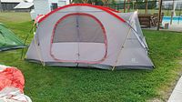 Side view of gray and red dome tent with mesh and fabric door, set up on grassy area.