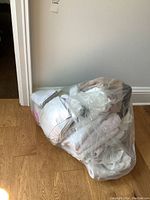 A plastic bag filled with assorted towels of varying sizes and colors placed on wooden floor against a wall.