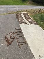 Full view of both sets of tractor chains laying on pavement and driveway, showing size difference and overall condition.