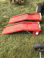 Two red steel vehicle ramps lying side by side on grass showing angled elevation and front stops.