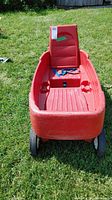 Front view of red Radio Flyer wagon showing ribbed seat, backrest, blue seatbelt, and front wheels on grass.