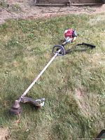 Full length view of trimmer laid on grass showing engine end, shaft, handle and cutting head