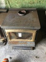 Top front view of steel wood stove with a rusted surface and round chimney outlet on top.