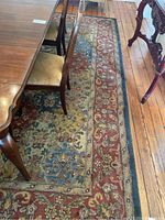 Wool rug partially under dining table with detailed floral and geometric pattern, showing wear and some dirt.