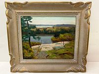 Frontal view of the oil on board painting in its gold decorative frame showing the full composition of lake, trees, rocky shore, and distant hills.