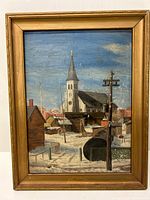 Framed oil painting on board showing a snowy Canadian village with church steeple, wooden buildings, utility poles, and a partly cloudy blue sky.