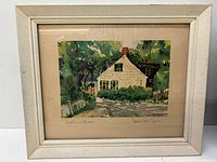 Full view of framed watercolor painting depicting a white house with green shutters, surrounded by trees, with a white picket fence and 'Go Slow Children' sign.