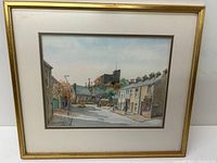 Full view of framed watercolour painting showing street, church, castle ruin, and buildings.