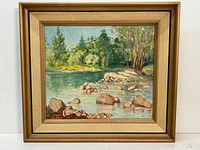 Framed oil painting of a river landscape with rocks and trees, showing the entire artwork with frame.
