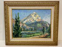 Framed oil painting of a snow-capped mountain with trees and greenery around a small body of water, signed by Aleen Aked in lower left corner.