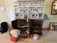 Front view of assembled dollhouse on wooden cabinet with drawers and doors; displays overall structure and included lower cabinet with storage boxes beneath