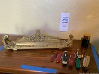 Ornate brass ink well with pocket cutting tools and Avon aftershave bottle on wooden surface